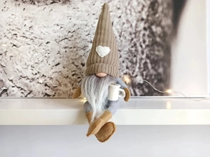 Close-up of a Christmas gnome with brown knitted heart hat holding a white coffee mug
