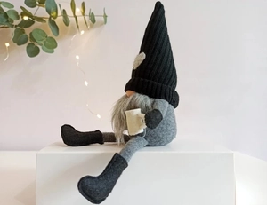 Macro view of a knitted Christmas gnome with long legs holding a white coffee mug