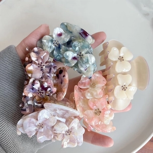 Hand holding floral acetate hair claws with rhinestones in multiple pearlescent colors