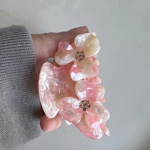Close-up of a pink floral acetate hair claw with sparkling rhinestones held by hand