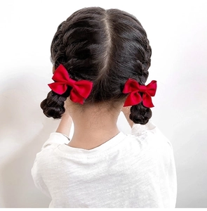 Close-up of red satin bow hair clips on a girl braided hair against a white background