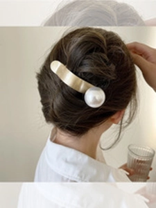 Dettaglio di un fermaglio per capelli dorato con una grande perla bianca su un'acconciatura
