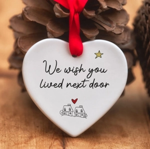Heart-shaped ceramic ornament with red ribbon and Christmas message on rustic background