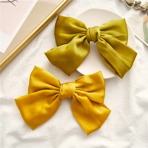Close-up of golden and mustard green satin bow hair clips on elegant white linen fabric