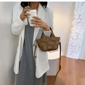 Close-up of a brown woven leather crossbody bucket bag shown with a white blazer outfit
