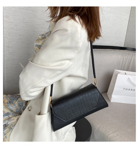 Detail of black faux crocodile leather crossbody bag with elegant gold hardware accents