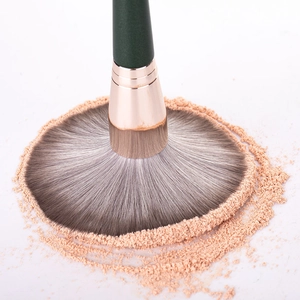 Close-up of a green fan makeup brush applying loose powder with soft bristles
