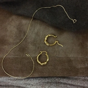 Close-up of golden twisted hoop earrings and minimalist link chain on a suede background