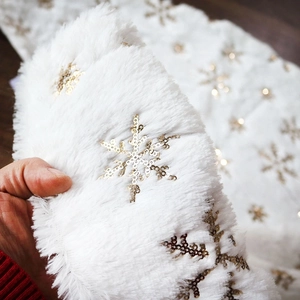 Detail of white faux rabbit fur Christmas tree skirt with gold sequin snowflakes