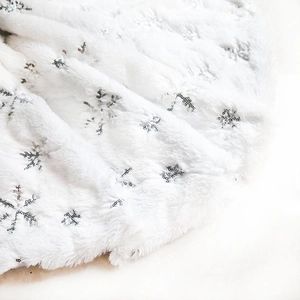 Close-up of white plush Christmas tree skirt with silver sequin snowflake patterns