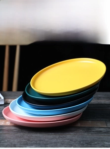 Stack of matte ceramic oval plates in six Nordic colors with smooth glazed finish