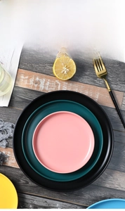 Top view of stacked matte ceramic dinner plates in pink, dark green, and black Nordic style