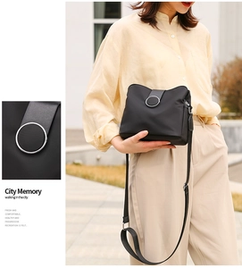 Detail of silver ring buckle on black nylon crossbody bag worn by a model in the city
