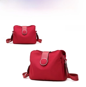Detail view of red nylon crossbody bag showing the round decorative buckle and wide strap