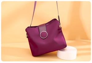 Detail of purple nylon crossbody bag with metal buckle on a white pedestal stand