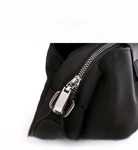 Close-up of smooth silver metal zippers on black nylon crossbody bag with twill texture