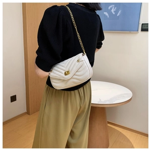 Detail of white quilted chain bag featuring V-shaped stitching and gold twist lock