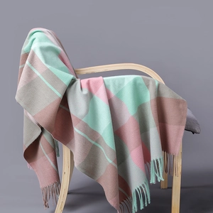 Plaid cashmere scarf in pink and mint green with tassels draped on a wooden chair