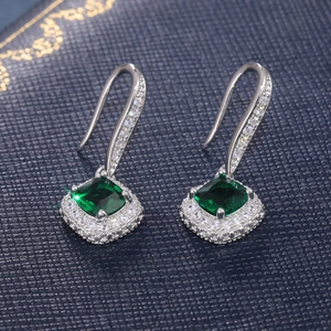 Macro detail of emerald-green cushion cut zircon earrings with silver halo drop hooks