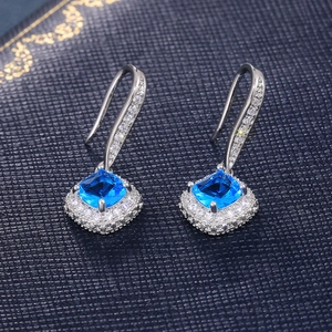 Macro detail of silver square blue zircon earrings with sparkling halo and hook setting