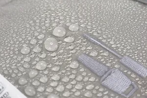 Macro shot of gray waterproof fabric with water droplets and detailed embroidery