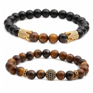 Dettaglio del set di bracciali con pietre occhio di tigre e ciondoli corona dorati su bianco