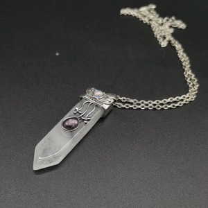 Detail of hexagonal crystal pendant with ornate silver metal filigree and purple gem