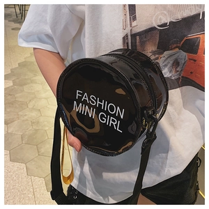 Detail of a black round patent leather crossbody bag with white fashion mini girl lettering