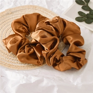 Glossy bronze satin hair scrunchies set on woven mat background for daily styling