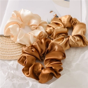 Detailed close-up of three satin scrunchies in cream, champagne, and bronze earth tones