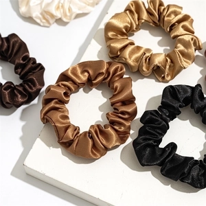 Close-up of high-gloss satin scrunchies in black, coffee, gold, and cream on a white stone