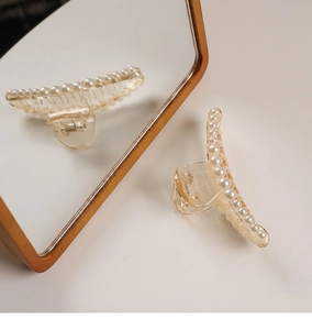 Macro shot of elegant champagne resin hair claw with inlaid pearls and gold spring