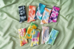 Flat lay of ten assorted cotton tie-dye mid-tube socks on a green fabric backdrop