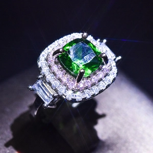 Close-up of luxury white gold ring with large emerald cut green gem and halo diamonds