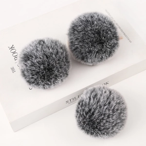 Three grey and white faux rabbit fur pom poms on a white book for fashion accessories