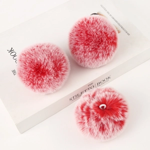Detail of three red and white gradient faux rabbit fur pompom charms on a white book