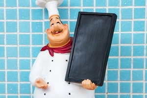 Close-up of chef figurine holding a black chalkboard for menus on blue mosaic background
