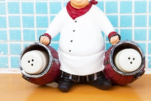 Detail view of a chef figurine holding salt and pepper shakers in rustic red buckets