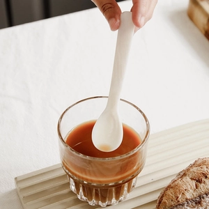 Hand holding white shell spoon for caviar or ice cream in a cozy tea time setting