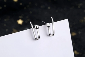 Macro shot of silver U-shaped ball earrings with polished metal texture on white card