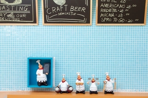 Detail of five vintage chef figurines holding kitchen tools on a rustic wooden shelf