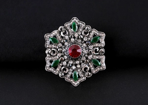 Detail of baroque brooch with red ruby center and green marquise gems on black fabric
