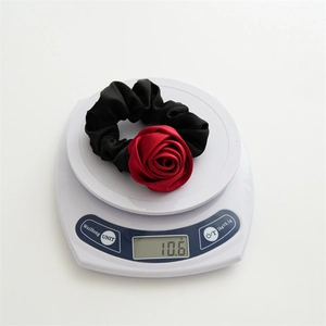 Satin fabric red rose scrunchie with elastic hair band displayed on a scale