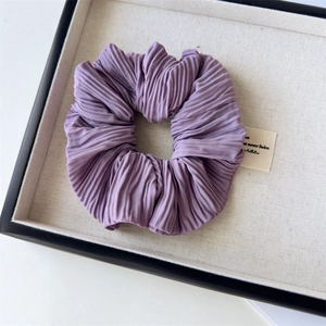Dettaglio di un elastico per capelli in tessuto plissettato viola con etichetta in scatola