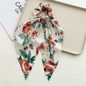 Close-up of floral satin scrunchie with long streamers in a minimalist tray