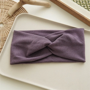 Detailed view of a purple fabric twist headband for women on a minimal beige background