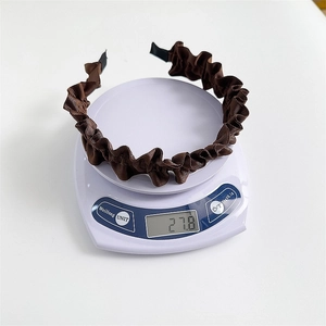 Brown pleated fabric headband weighing 27.8g on a digital scale for lightweight comfort