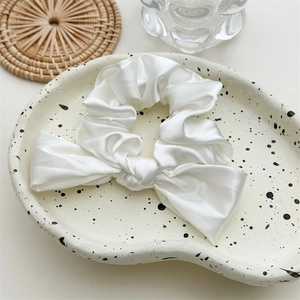 Detail shot of a white satin scrunchie with a bow on a ceramic dish with rustic decor