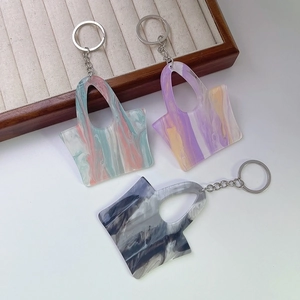 Three creative acrylic handbag keychains with colorful marble textures on a wooden tray