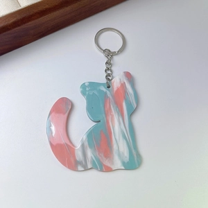 Detail of a cat-shaped acrylic keychain with pink and blue marble pattern on white background